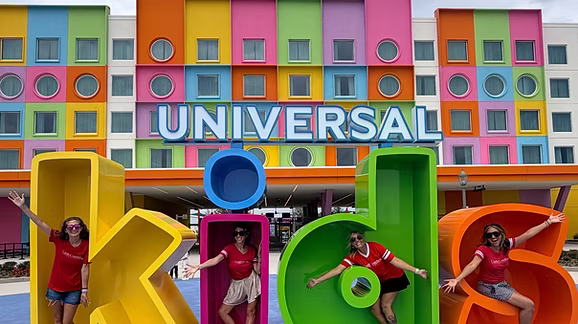 Castle Coaches Travel advisors pose inside the colorful Universal Kids letters in front of Universal Kids Resort in Frisco, Texas. The vibrant entrance showcases the family-focused theme park designed for younger children, making it a fun destination for preschoolers and elementary-aged kids visiting North Texas.